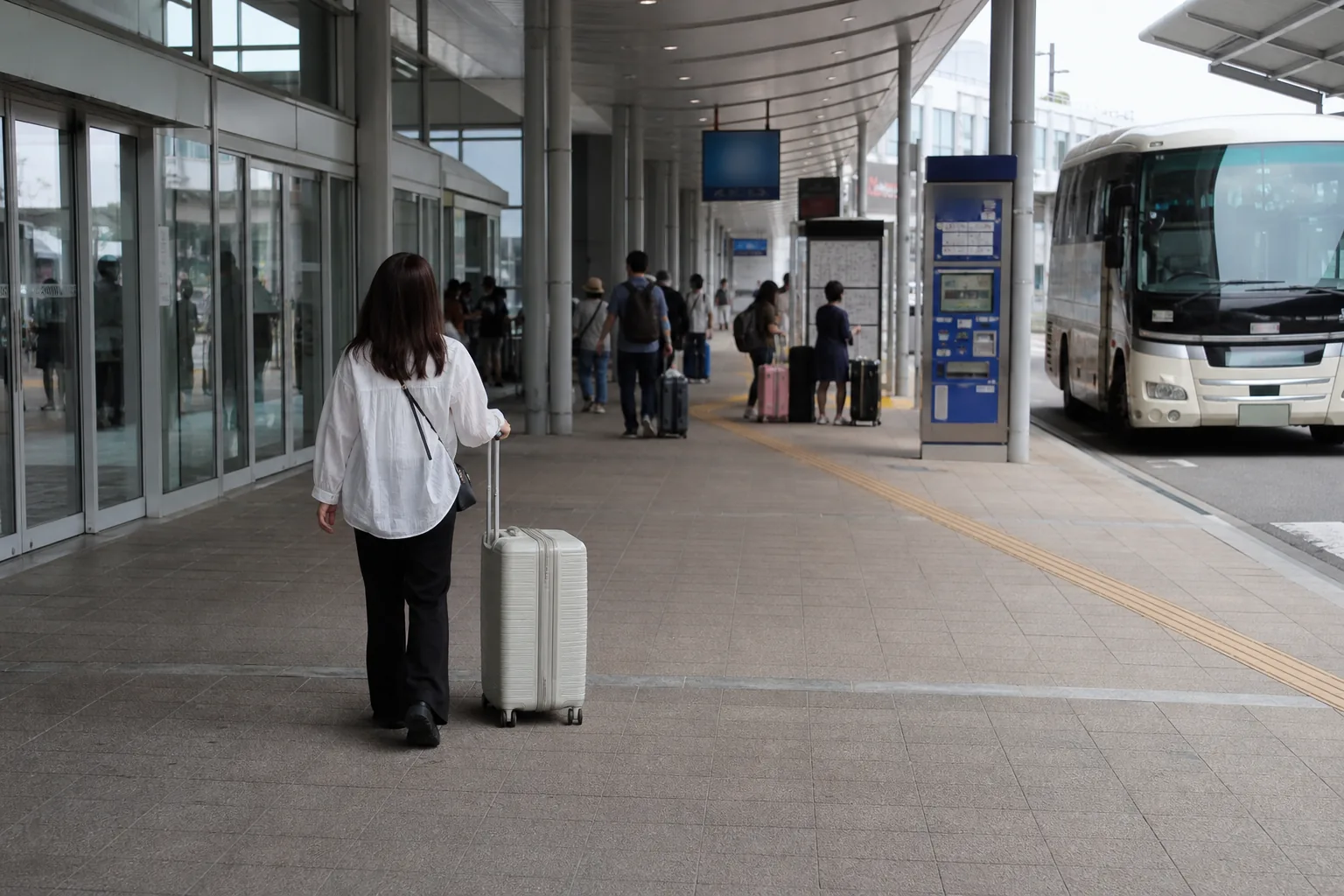 간사이공항 제1터미널 1층 리무진버스 승차장과 자동 발매기 앞을 캐리어를 끌고 지나가는 여행객